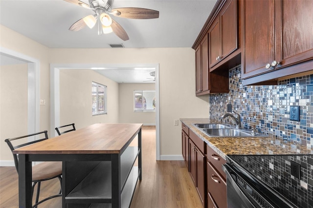 kitchen with a kitchen breakfast bar, ceiling fan, dark stone countertops, and sink