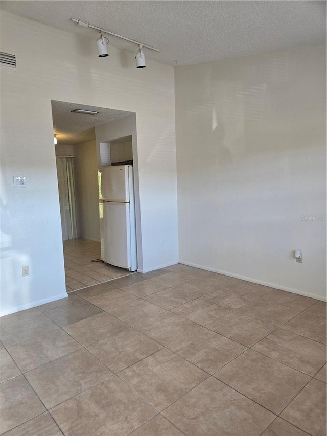 empty room with light tile patterned floors, a textured ceiling, and track lighting