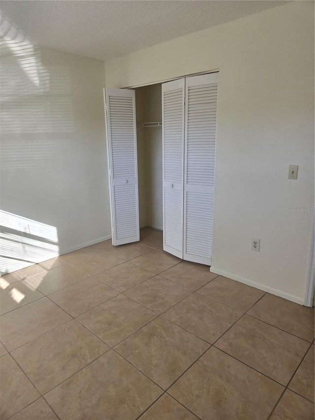 unfurnished bedroom featuring light tile patterned flooring, a textured ceiling, and a closet