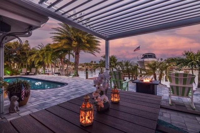 pool at dusk featuring a patio area, a water view, and an outdoor fire pit