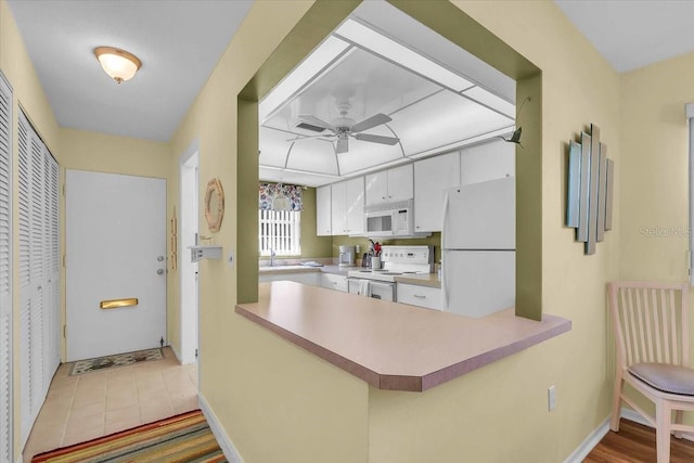 kitchen featuring white appliances, sink, kitchen peninsula, ceiling fan, and white cabinetry