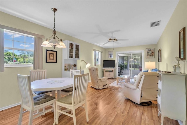 dining space with ceiling fan with notable chandelier, light hardwood / wood-style floors, and a wealth of natural light