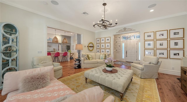 living room with ornamental molding, a chandelier, and light hardwood / wood-style flooring