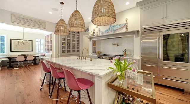 kitchen featuring pendant lighting, a kitchen island with sink, light stone counters, a kitchen bar, and decorative backsplash