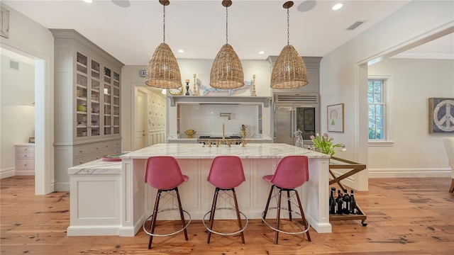 kitchen with light stone counters, a spacious island, stainless steel built in refrigerator, and a kitchen breakfast bar