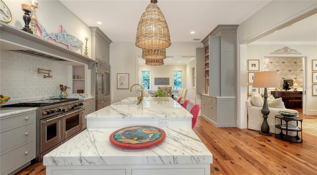 kitchen with gray cabinetry, premium appliances, an island with sink, light stone countertops, and decorative backsplash