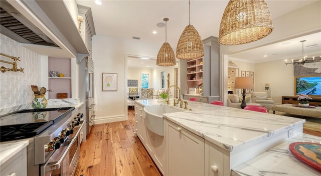 kitchen with pendant lighting, sink, light stone counters, premium appliances, and a center island with sink