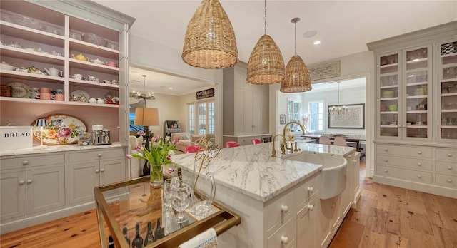 kitchen with light hardwood / wood-style flooring, a kitchen island with sink, hanging light fixtures, an inviting chandelier, and light stone counters