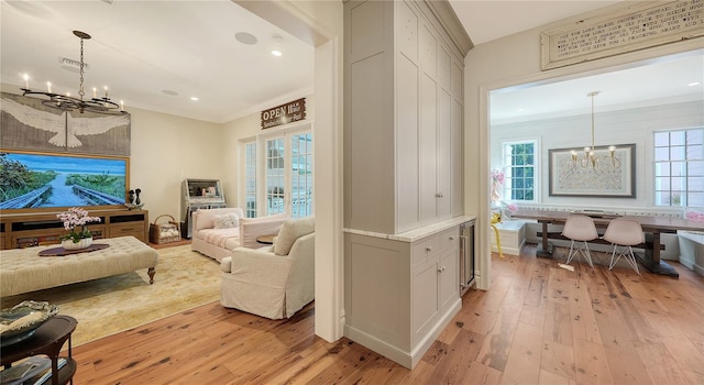 living room featuring crown molding, plenty of natural light, light wood-type flooring, and a notable chandelier