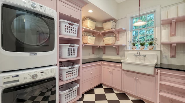 washroom with sink, cabinets, and stacked washer and clothes dryer