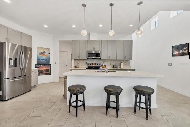 kitchen featuring a kitchen breakfast bar, sink, gray cabinets, an island with sink, and appliances with stainless steel finishes