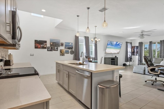 kitchen with ceiling fan with notable chandelier, stainless steel appliances, sink, pendant lighting, and an island with sink