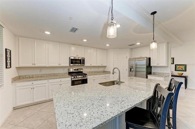 kitchen with stainless steel appliances, sink, a large island with sink, decorative light fixtures, and white cabinetry