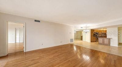 unfurnished living room with an inviting chandelier, light wood-style flooring, and visible vents