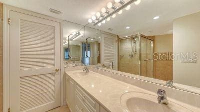 bathroom with visible vents, a sink, a shower stall, and double vanity