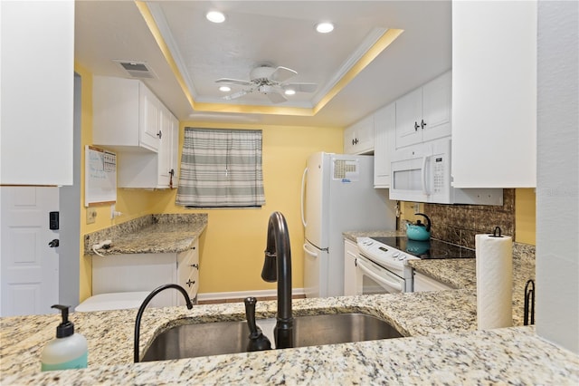 kitchen with ornamental molding, white appliances, a raised ceiling, ceiling fan, and white cabinets