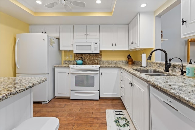 kitchen with a raised ceiling, sink, white cabinets, and white appliances