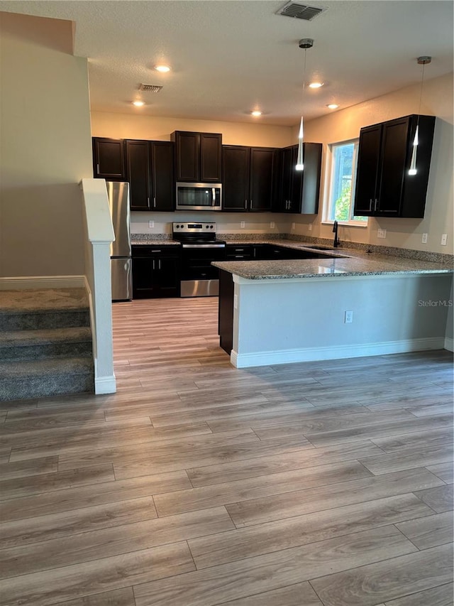 kitchen with kitchen peninsula, pendant lighting, stainless steel appliances, and sink