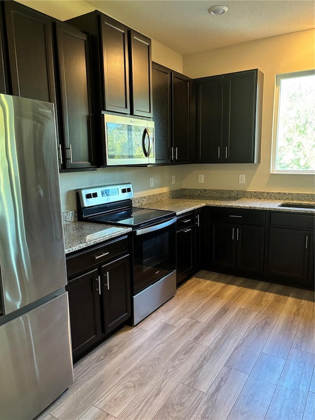 kitchen with appliances with stainless steel finishes, sink, light stone countertops, and light hardwood / wood-style floors