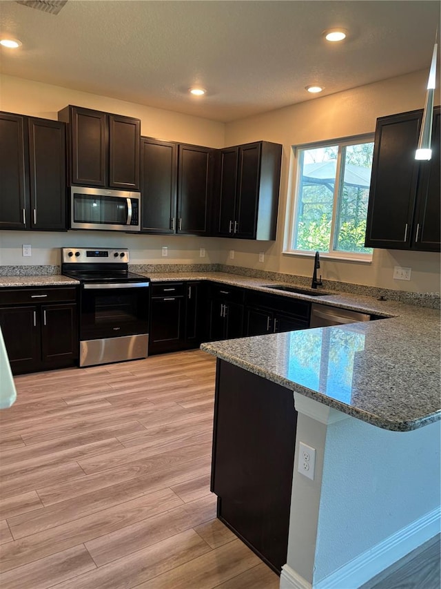 kitchen featuring sink, kitchen peninsula, stainless steel appliances, light stone countertops, and light wood-type flooring