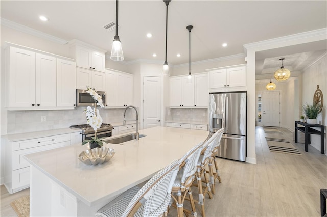 kitchen featuring appliances with stainless steel finishes, decorative light fixtures, white cabinetry, and a kitchen island with sink