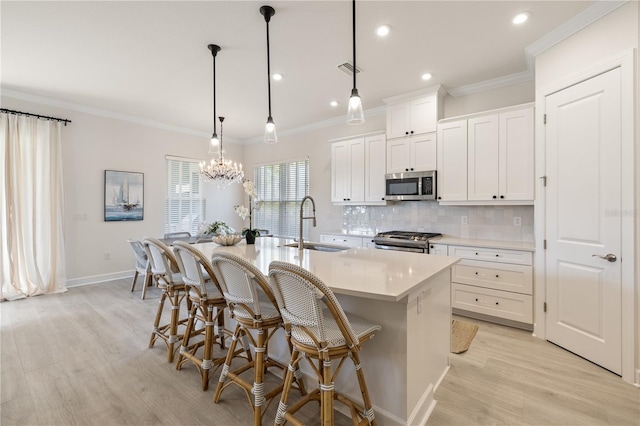 kitchen featuring appliances with stainless steel finishes, a kitchen island with sink, sink, pendant lighting, and white cabinetry