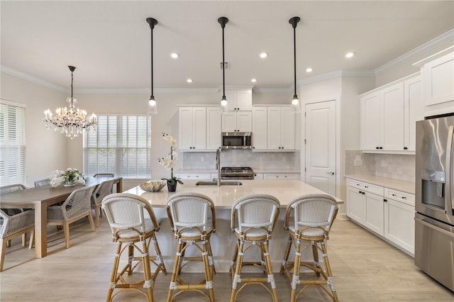 kitchen featuring appliances with stainless steel finishes, backsplash, a center island with sink, white cabinets, and hanging light fixtures