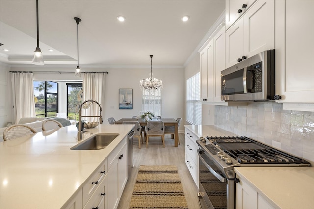 kitchen featuring stainless steel appliances, crown molding, sink, white cabinets, and hanging light fixtures