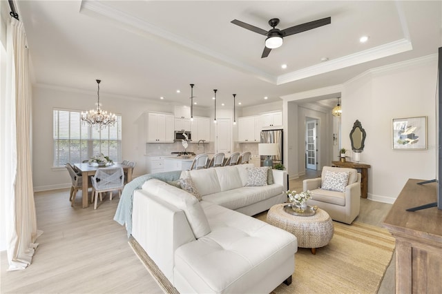 living room with ceiling fan with notable chandelier, light wood-type flooring, crown molding, and a tray ceiling