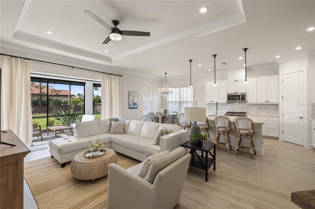 living room featuring ceiling fan with notable chandelier, a raised ceiling, and plenty of natural light