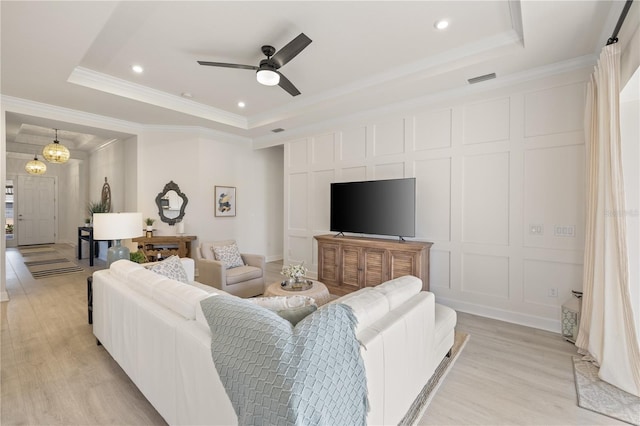 living room featuring a tray ceiling, ceiling fan, crown molding, and light hardwood / wood-style floors