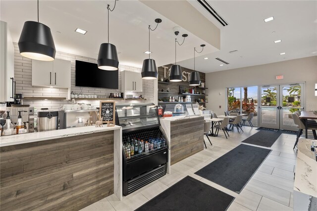 kitchen featuring decorative backsplash, french doors, hanging light fixtures, and light stone counters