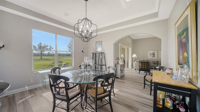 dining space with a tray ceiling, light wood-type flooring, and an inviting chandelier