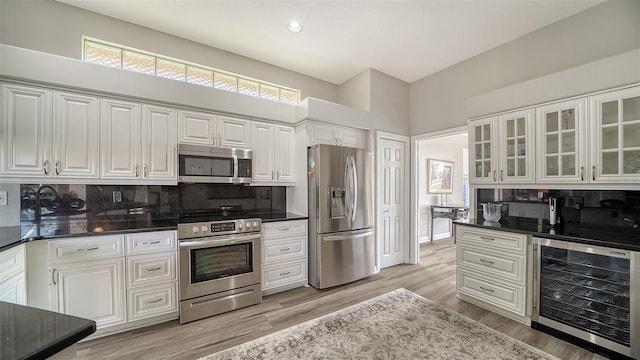 kitchen featuring stainless steel appliances, a high ceiling, wine cooler, decorative backsplash, and white cabinets