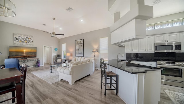 kitchen featuring backsplash, high vaulted ceiling, appliances with stainless steel finishes, a kitchen bar, and white cabinetry