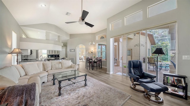 living room with ceiling fan with notable chandelier, lofted ceiling, a wealth of natural light, and light hardwood / wood-style flooring