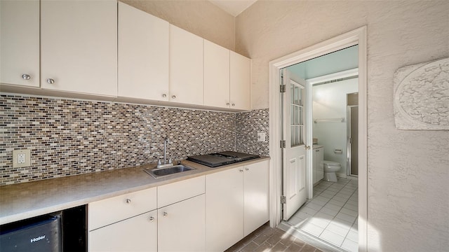 kitchen with backsplash, black gas stovetop, sink, light tile patterned floors, and white cabinets