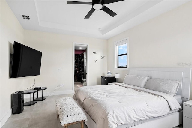 bedroom featuring a walk in closet, a tray ceiling, and ceiling fan