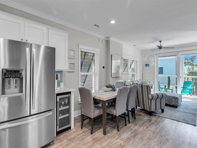 dining area with light wood-type flooring, beverage cooler, crown molding, and ceiling fan