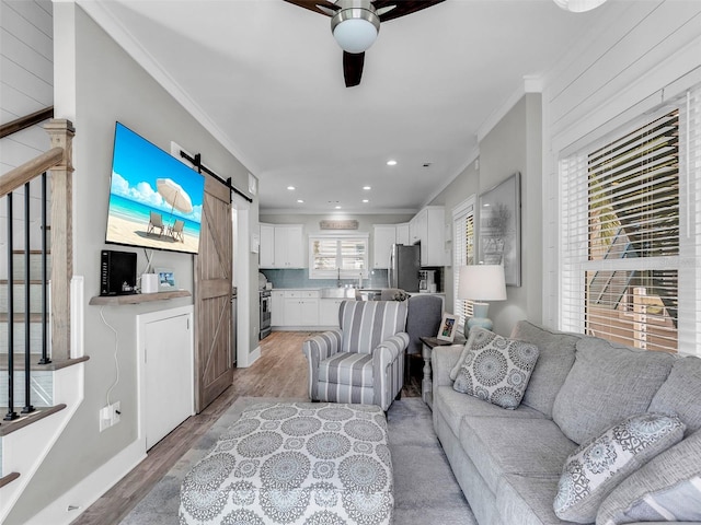 living room with a barn door, ceiling fan, light hardwood / wood-style floors, and ornamental molding