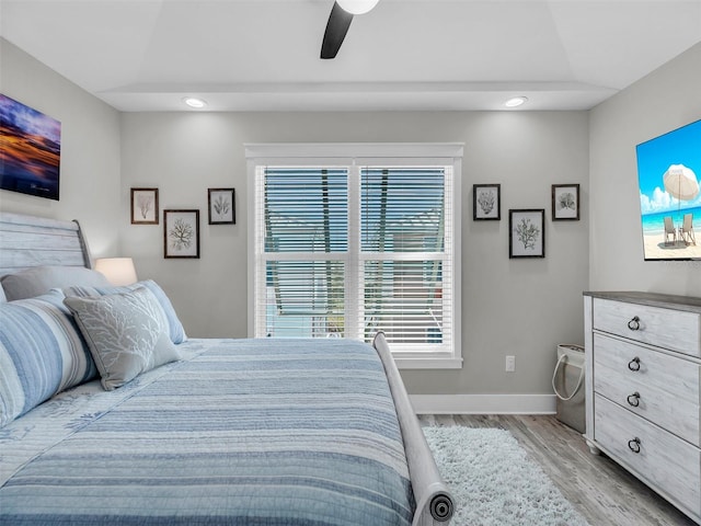 bedroom with ceiling fan, a raised ceiling, and light hardwood / wood-style flooring