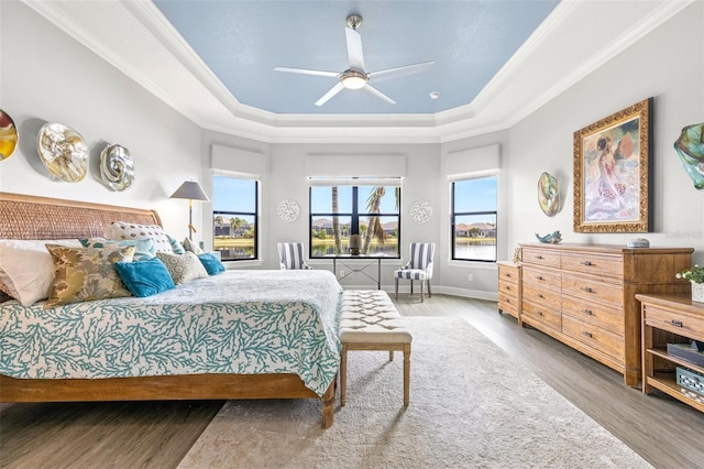 bedroom with hardwood / wood-style floors, ceiling fan, a raised ceiling, and multiple windows