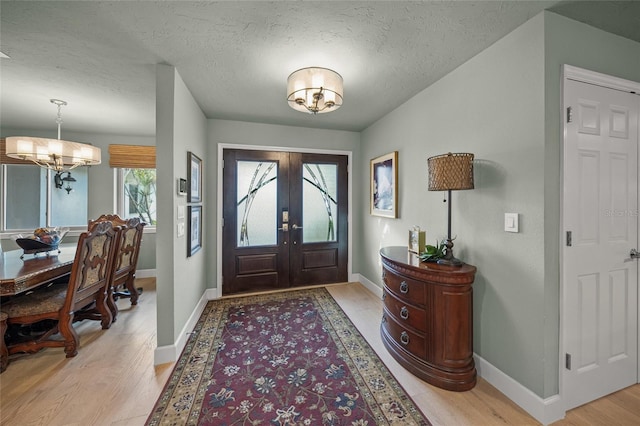 entryway with a textured ceiling, a chandelier, light hardwood / wood-style flooring, and french doors