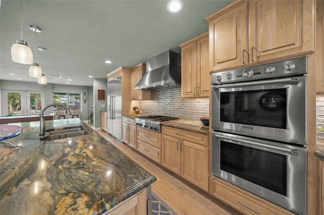 kitchen featuring sink, stainless steel appliances, wall chimney range hood, dark stone counters, and pendant lighting