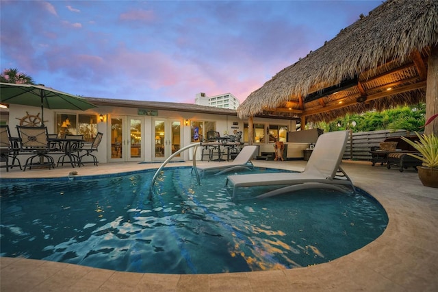 pool at dusk featuring french doors and a patio