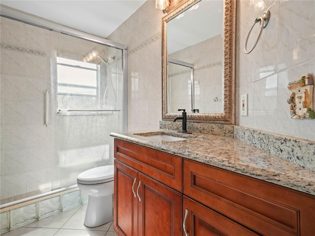 bathroom with vanity, a shower with door, tile patterned flooring, toilet, and tile walls