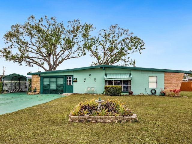 back of property with driveway, a carport, concrete block siding, and a lawn