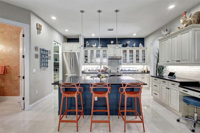 kitchen featuring hanging light fixtures, decorative backsplash, high quality fridge, a kitchen island, and a kitchen bar