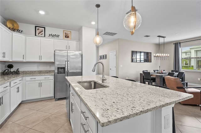 kitchen with sink, decorative light fixtures, white cabinets, and an island with sink