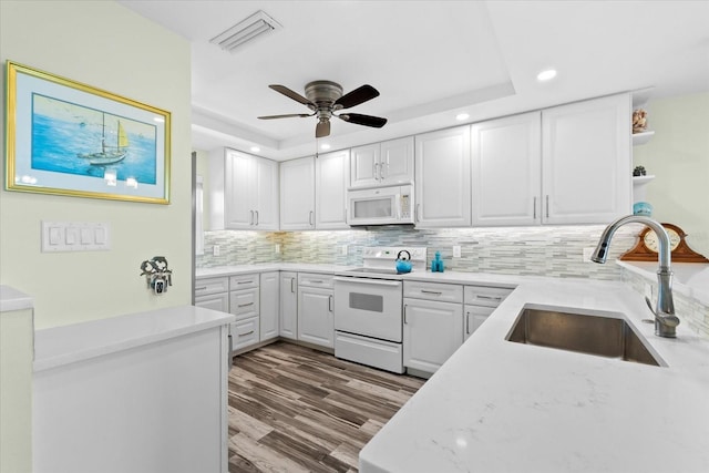 kitchen featuring white appliances, a tray ceiling, sink, light hardwood / wood-style flooring, and white cabinets